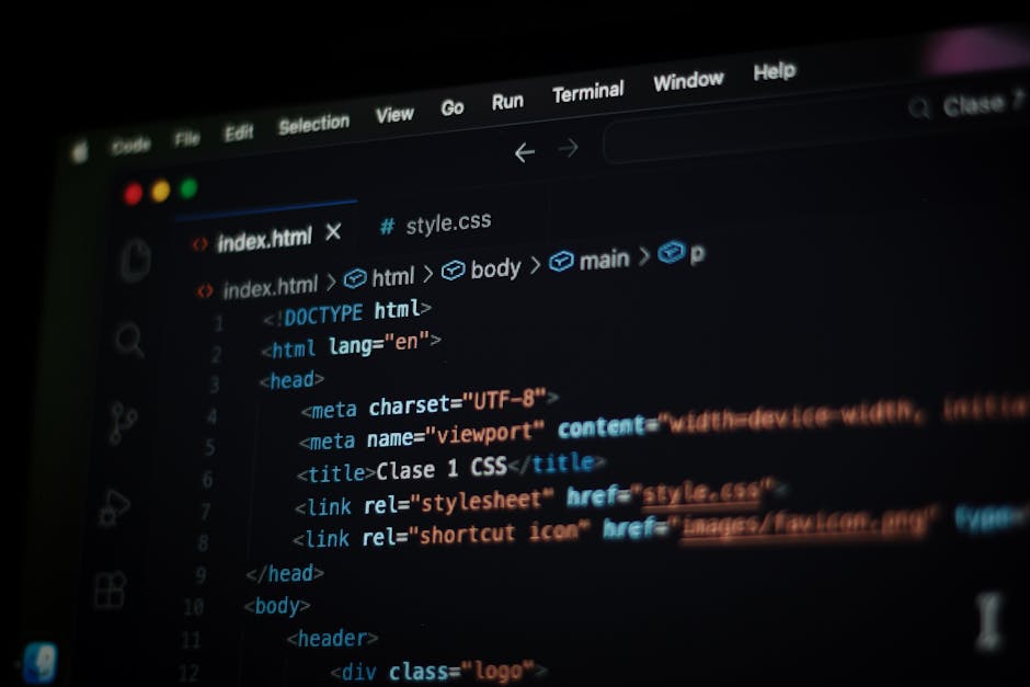 Close-up photograph of a computer screen displaying lines of coloured HTML or CSS code in a dark environment, with syntax highlighting in shades of blue, yellow, red, and white. The code appears to be